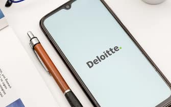 In this photo illustration a Deloitte logo seen displayed on a smartphone screen on a desk next to a cafe, a pen, glasses and a magazine in Athens, Greece on June 27, 2022.  (Photo by Nikolas Kokovlis/NurPhoto via Getty Images)