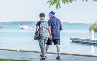 Senior couple walk hand in hand along the boardwalk at the waterfront in Orillia Ontario Canada.