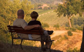 Couple sits on bench overlooking fields and vineyards near Villa Rosa agriturisimo Panzano in Chianti Italy no release avail