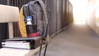 A students full backpack complete with water bottle on a bench seat with an organized ring binder folder full of school books and notes. High school e