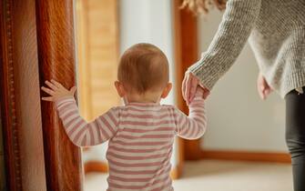 young child assisted by mother or nanny indoor home wearing striped onesie medium close up of hands and back of unsure baby