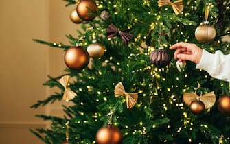 Woman's hands decorating New Year illuminating fir tree with vintage Christmas baubles.