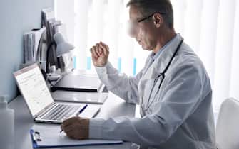 Serious older doctor using laptop computer in medical office.