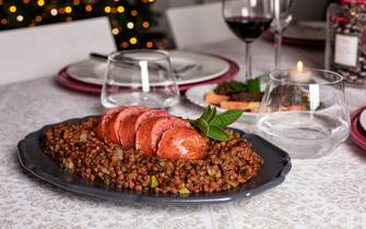An Italian New Year Eve table. Traditional cotechino con lenticchie or pork sausage with Lentils cooked with vegetables. Red wine in glasses. Traditional Festive table.