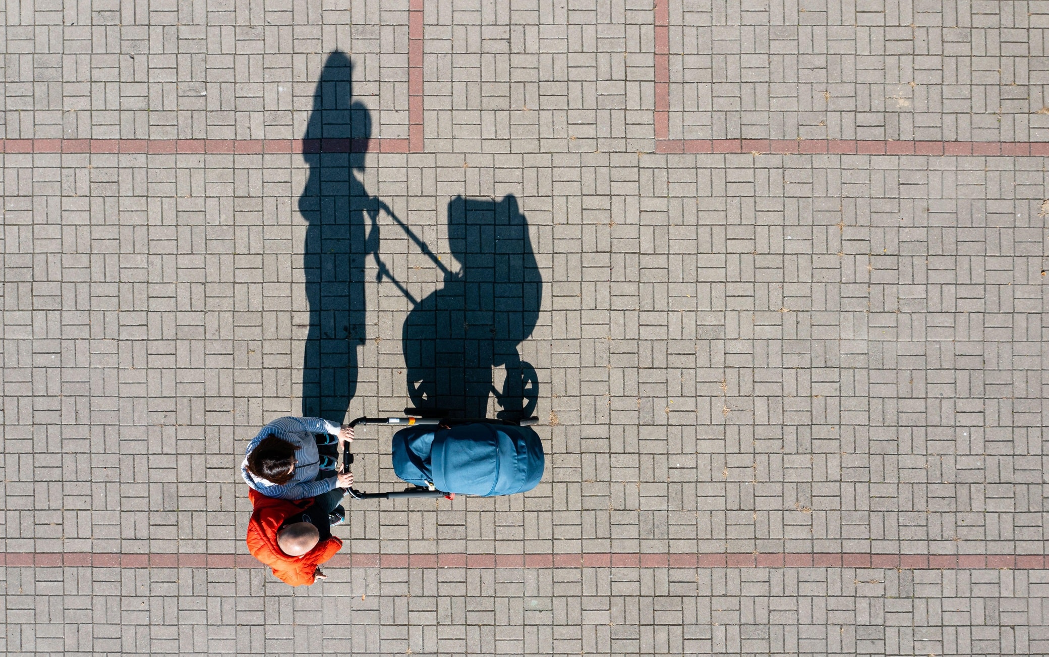 Aerial view of parent with a stroller on a walk during sunny day, perspective directly above