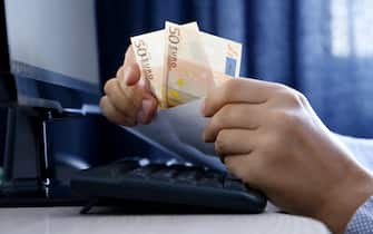 Envelope with euro banknotes in male hands. Man pulls money out of an envelope on PC keyboard background, wages, bonus or bribe concept