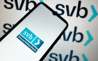 In this photo illustration the Silicon Valley Bank logo seen displayed on a smartphone screen and in the background in Chania, Greece on March 10, 2023. Shares in banks around the world have slid after troubles at one US bank triggered fears of a wider problem for the financial sector. (Photo Illustration by Nikolas Kokovlis/NurPhoto via Getty Images)