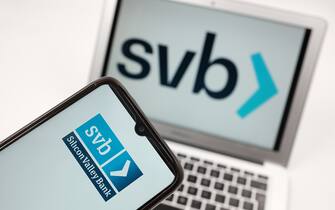In this photo illustration the Silicon Valley Bank logo seen displayed on a smartphone screen and in the background in Chania, Greece on March 11, 2023. Shares in banks around the world have slid after troubles at one US bank triggered fears of a wider problem for the financial sector. (Photo illustration by Nikolas Kokovlis/NurPhoto via Getty Images)