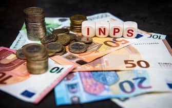 banknotes and coins of euro on a dark background and written INPS Italian pension institution