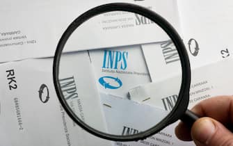 Carrara, Italy - December 06, 2021 - Man highlights the INPS (National Social Security Institute) logo with a magnifying glass