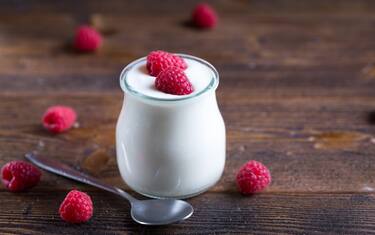 White yogurt with raspberries in glass bowl on rustic table.