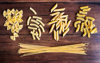 Variety of types and shapes of dry Italian pasta - fusilli, spaghetti, farfalle and penne, top view. Uncooked whole wheat italian pasta. Image with copy space.