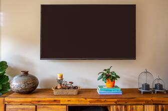 A wall mounted TV above a sideboard with decorative, metallic urn and other decor items sitting on a wooden sideboard.