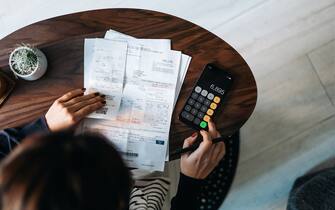 Overhead view of young Asian woman managing personal banking and finance at home. Planning budget and calculating expenses while checking her bills with calculator. Managing taxes and financial bills. Home budgeting. Concept of finance and economy