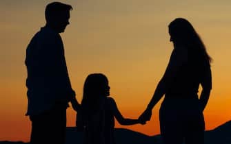 Silhouettes of family of mom dad and daughter standing on the seashore at sunset