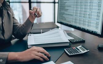 Investors working on desk office and check data cost, balance, profit and  currency on monitor screen. Accounting and  Financial concept.