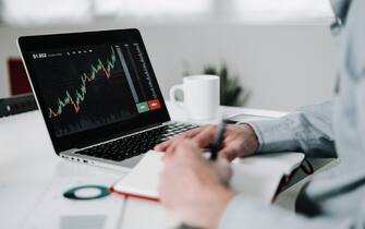 Young businessman using laptop for analyzing data stock market. He is working from home office - Stock market, investment and cryptocurrencies concept