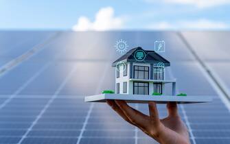 An architectural model with solar panels . concept energy saving and sustainable resource . The model of house lift by hand on the solar panel with digitization display , Photovoltaic against with sun  light and reflex on solar panel .