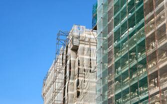 Works for adaptation and energy saving of buildings in Italy. Low angle view of two tall building with scaffolding in front of the facades.
