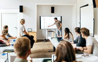 A student giving a presentation to the class during a seminar session and using a large monitor as a visual aid.