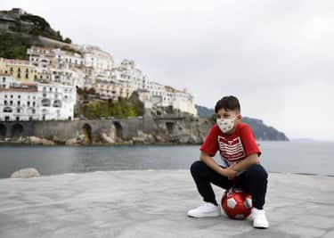 AMALFI, ITALY - MAY 13: A boy with a mask against covid 19 infection plays football at Amalfi's port on May 13, 2020 in Amalfi, Italy. Italy was the first country to impose a nationwide lockdown to stem the transmission of the Coronavirus (Covid-19), and its restaurants, theaters and many other businesses remain closed. (Photo by Francesco Pecoraro/Getty Images)