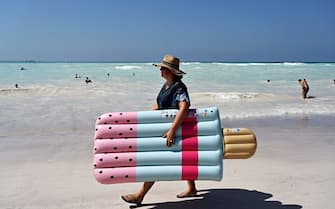 A woman holds an ice cream inflatable mattress as she walks on the "Spiagge Bianche" (white sand) beach in Rosignano Solvay, a town in Italy's central Tuscany region, on July 31, 2019. - The white sand and unusual Caribbean appearance is not natural, but due to production waste from the Solvay chemical plant in Rosignano Solvay, which produces basic chemical products such as sodium carbonate, bicarbonate, hydrogen peroxide, calcium chloride and chlorine. (Photo by Vincenzo PINTO / AFP)        (Photo credit should read VINCENZO PINTO/AFP via Getty Images)