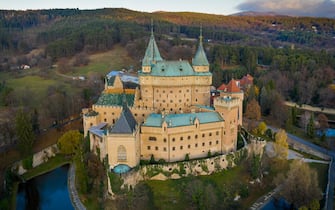 Bojnice castle in Slovakia from a high view with moat and greenery around and forest in the background. European medieval 12th century fort.