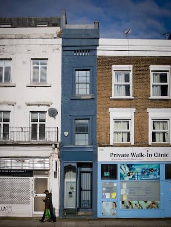 A pedestrian passes the front of what is dubbed 'London's thinnest house' (painted blue) in west London on February 5, 2021. - Wedged neatly between a doctor's surgery and a shuttered hairdressing salon, the five floor house in Shepherds Bush is just 5ft 6ins (1.6 metres) at its narrowest point and is currently on the market for £950,000 ($1,300,000, 1,100,000 euros). The unusual property, originally a Victorian hat shop with storage for merchandise and living quarters on its upper floors, was built sometime in the late 19th or early 20th century. (Photo by Tolga Akmen / AFP) (Photo by TOLGA AKMEN/AFP via Getty Images)