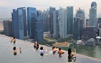 This photo taken on June 13, 2018 shows people using their phones to take photos in the rooftop pool of the Marina Bay Sands resort hotel, which overlooks the financial district skyline of Singapore. (Photo by Anthony WALLACE / AFP) (Photo by ANTHONY WALLACE/AFP via Getty Images)