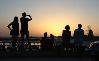 837971408 People enjoy sunset in front of windmills and salternes on August 15, 2017 in Marsala, Sicily. (Photo by ludovic MARIN / AFP) (Photo credit should read LUDOVIC MARIN/AFP via Getty Images)