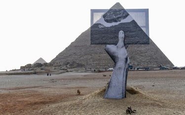 A picture shows a view of an art installation an installation entitled 'Greetings From Giza' by French artist and photographer Jean Rene, better known as JR, in front of the pyramids at the ancient Giza necropolis on the western outskirts of the Egyptian capital's twin city of Giza, on October 23, 2021. - The installation is part of an exhibition entitled 'Forever is Now' organized by Art DEgypte including large-scale sculptures and installations by ten international contemporary artists. - XGTY / RESTRICTED TO EDITORIAL USE - MANDATORY CREDIT "AFP PHOTO / ART D EGYPTE  - NO MARKETING NO ADVERTISING CAMPAIGNS - DISTRIBUTED AS A SERVICE TO CLIENTS - RESTRICTED TO EDITORIAL USE - MANDATORY MENTION OF THE ARTIST UPON PUBLICATION - TO ILLUSTRATE THE EVENT AS SPECIFIED IN THE CAPTION (Photo by Ahmed HASAN / AFP) / XGTY / RESTRICTED TO EDITORIAL USE - MANDATORY CREDIT "AFP PHOTO / ART D EGYPTE  - NO MARKETING NO ADVERTISING CAMPAIGNS - DISTRIBUTED AS A SERVICE TO CLIENTS - RESTRICTED TO EDITORIAL USE - MANDATORY MENTION OF THE ARTIST UPON PUBLICATION - TO ILLUSTRATE THE EVENT AS SPECIFIED IN THE CAPTION / XGTY / RESTRICTED TO EDITORIAL USE - MANDATORY CREDIT "AFP PHOTO / ART D EGYPTE  - NO MARKETING NO ADVERTISING CAMPAIGNS - DISTRIBUTED AS A SERVICE TO CLIENTS - RESTRICTED TO EDITORIAL USE - MANDATORY MENTION OF THE ARTIST UPON PUBLICATION - TO ILLUSTRATE THE EVENT AS SPECIFIED IN THE CAPTION (Photo by AHMED HASAN/AFP via Getty Images)