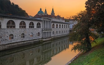 Slovenia, Ljubljana, Plecnik Colonnade and Central Market at sunset with the Cathedral of St Nicholas behind and the Ljubljanica River in the foreground.