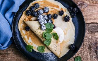 Delicious summer treat, healthy vegetarian breakfast with crepes, fresh blackberries and sour cream served in rural cast iron skillet, top view
