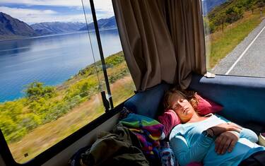 Girl asleep in the back of a campervan driving along the road between Queenstown and Glenorchy, South Island, New Zealand. The mountains rising from Lake Wakatipu are visible through the window behind her. | Location: Glenorchy, South Island, New Zealand.  (Photo by In Pictures Ltd./Corbis via Getty Images)