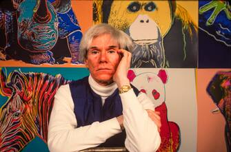 American Pop artist Andy Warhol (1928 - 1987) sits in front of several paintings in his 'Endangered Species' at his studio, the Factory, in Union Square, New York, New York, April 12, 1983. (Photo by Brownie Harris/Corbis via Getty Images)