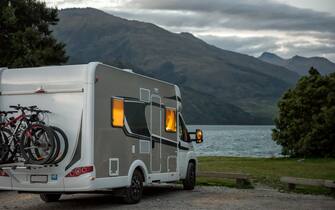 European style motorhome with interior lights on, parked at dusk at the Boundary Creek Campsite, next to Lake Wanaka in South Westland, New Zealand.
