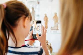 A young girl taking some photos of an exhibit using her smartphone while on a field trip with her  classmates.
