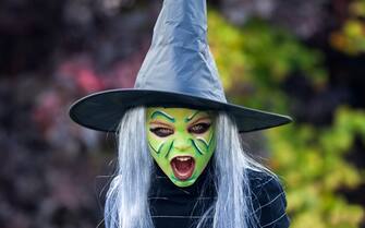 Screaming little girl dressed up as witch complete with hat, gray wig and green face paint.