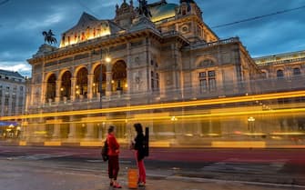 A women chat at the tram stop in front of the lit-up Wiener Staatsoper ,Vienna's State Opera, during the twilight in the city center of Vienna, on August 12,2014.The Vienna State Opera is an opera house  and opera company  with a history dating back to the mid-19th century. It was originally called the Vienna Court Opera (Wiener Hofoper) but in 1920, with the replacement of the Habsburg Monarchy by the First Republic of Austria, it was renamed to the Vienna State Opera. The members of the Vienna Philharmonic are recruited from its orchestra.AFP PHOTO/JOE KLAMAR        (Photo credit should read JOE KLAMAR/AFP via Getty Images)