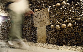 A visitor walks past skulls and bones from the defunct Holy Innocents' Cemetery now stacked at the Catacombs of Paris on October 14, 2014. These underground quarries were used to store the remains of generations of Parisians in a bid to cope with the overcrowding of Paris' cemeteries at the end of the 18th century, and are now a popular tourist attraction. AFP PHOTO / PATRICK KOVARIK        (Photo credit should read PATRICK KOVARIK/AFP via Getty Images)
