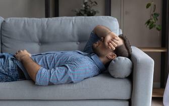 Stressed young man sleeping on sofa at home.