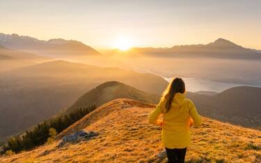 Rear view of woman with yellow jacket gazing at mountains and northern branch of Lake Como at dawn. Peglio, Como province, Lombardy region, Italy.