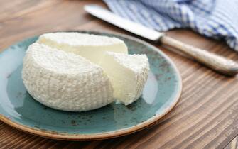 Fresh ricotta on plate on wooden background