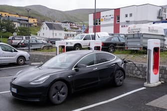 Honningsvag, Norway - July 26, 2022: A static shot of a solid black Tesla Model 3 dual motor charging at the Honningsvag Supercharger in a cloudy summ