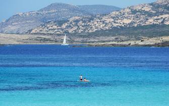 Scenic view of the Asinara island coastline on a summer day with a white sailboat in the beautiful turquoise Mediterranean sea
