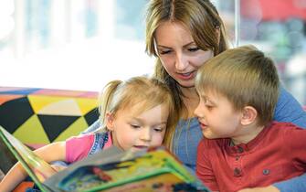Portrait of pretty young women reading fairy tales with two children in the children's playroom