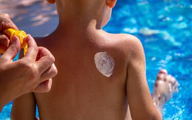 Mother puts cream on her son's back. Caring for baby skin. Sunscreens in the travel