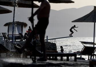 A boy jumps in the Adriatic sea as the sun sets on the beach of Radhima, near Vlora, on June 26, 2021 as a heat wave hit Albania and temperatures reach a peak of 42 degrees Celsius. (Photo by Gent SHKULLAKU / AFP) (Photo by GENT SHKULLAKU/AFP via Getty Images)