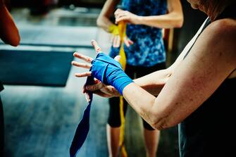 Senior woman wrapping hands before boxing workout in gym