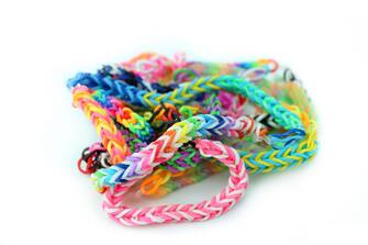 Photo showing a pile of rainbow coloured loom bracelets, made from coloured rubber loom bands.  These friendship bracelets are popular with young children, who weave the rubber bands together using a simple plastic loom device.